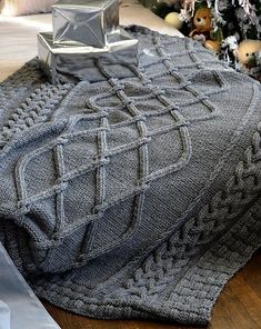 a knitted blanket on the floor next to a christmas tree with presents and other decorations