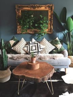 a living room filled with lots of plants next to a wooden table and mirror on the wall