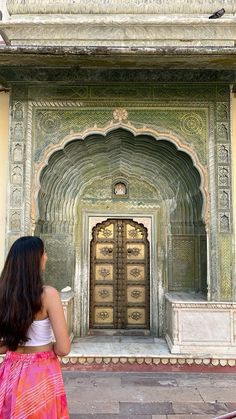 a woman standing in front of a building with an ornate doorway and door, looking into the distance