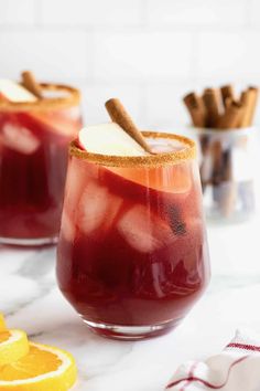 two glasses filled with red wine and cinnamon garnish on top of a marble counter