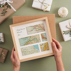 a person holding up a framed map in front of presents and wrapped gifts on a table