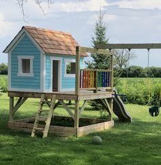 a small blue house with a swing set in the grass and a tree behind it