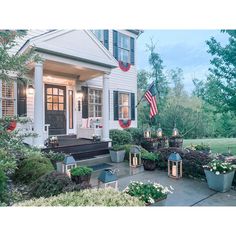 an american flag hangs on the front door of a white house with potted plants