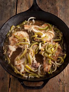 a skillet filled with meat and onions on top of a wooden table