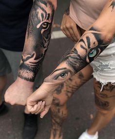 two people holding hands with tattoos on their arms and one has a tiger's eye