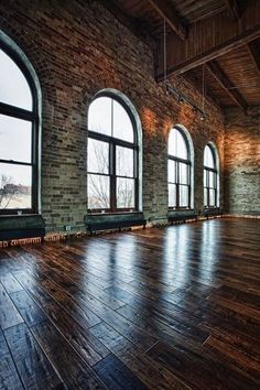 an empty room with wooden floors and large windows in the center, surrounded by brick walls