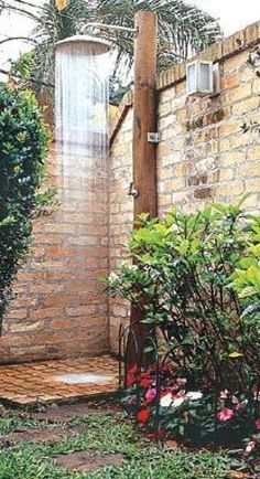 an outdoor shower in the middle of a garden with flowers and trees around it, next to a brick wall