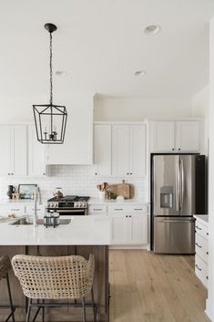 a kitchen with white cabinets and an island in front of a refrigerator freezer that has a light fixture hanging from it's ceiling