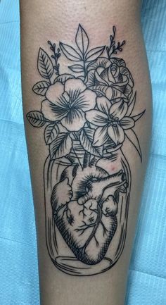 a black and white tattoo on the leg of a woman with flowers in a jar