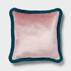 a pink and teal velvet pillow with fringe trim on the bottom, against a white background