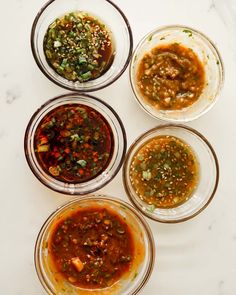 four glass bowls filled with different types of sauces on a white counter top next to each other