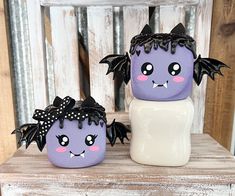 two purple and white ceramic pumpkins with bats on them sitting on a wooden table