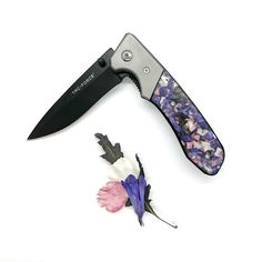 a knife is laying next to a flower on a white surface with purple and pink petals