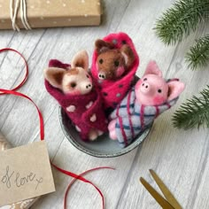 three small stuffed animals are sitting in a tin on a table next to christmas decorations