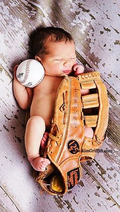 a baby is laying in a baseball mitt with a ball on his chest and it's head resting on the glove