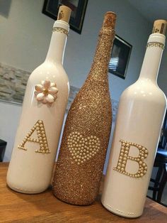 three white bottles with gold glitter letters and flowers on them sitting on a wooden table