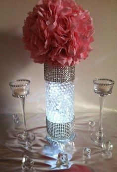 a vase filled with pink flowers next to two wine glasses and candle holders on a table