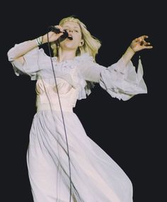 a woman in a white dress singing into a microphone