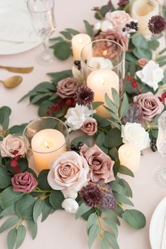 an arrangement of flowers and candles on a white table cloth with place settings for the centerpieces