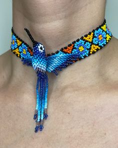 a woman wearing a blue and yellow beaded necklace with a bird on it's neck