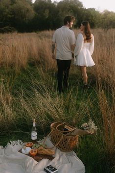 a man and woman standing next to each other in a field with food on the ground