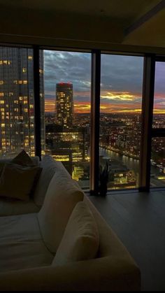 a living room filled with furniture next to tall buildings at night, looking out onto the city