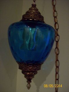 a blue glass lamp hanging from a chain on a wall in a room with white walls