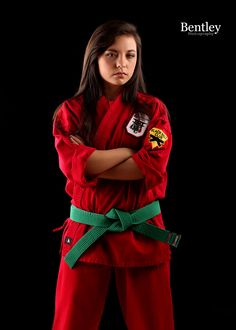 a woman in red is posing with her arms crossed and looking at the camera while wearing a green belt