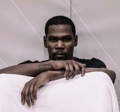 a man sitting on top of a white towel under a light colored background with his arms crossed