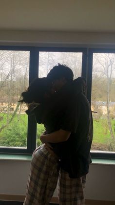 a man and woman hug in front of a window with the view of trees outside