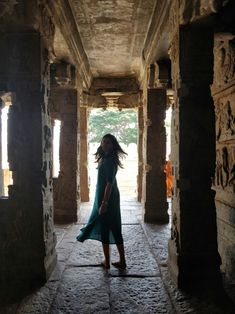 a woman in a long green dress walking through an ancient building with columns and arches