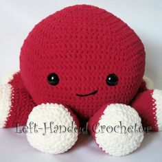 a crocheted red and white stuffed animal with black eyes sitting on a white surface