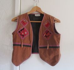 Lovely truly vintage Indian cotton vest. Earthy rust brown cotton with purple and black lining and trim. Sewn on each breast and on the back are squares of Indian mirrored fabric in colorful patterns. Two tassels on the front. Estimated era 60's. Vest is in very good vintage condition, with some light discoloration. The most prominent is on the right bottom front (see last photo) although it's not too bad overall. Otherwise good for it's age, no holes or other damage. Size is modern XS, arm holes are tight. Measurements taken flat in inches: pit to pit 18 arm holes 9  total length 18 Retro Brown Cotton Vest, Bohemian Cotton Vest For Fall, Bohemian Brown Vest Top, Fall Bohemian Cotton Vest, Bohemian Brown Vest For Festival, Fitted Brown Bohemian Vest, Vintage Brown Cotton Vest, Fitted Brown Festival Vest, Bohemian Brown Vest For Fall