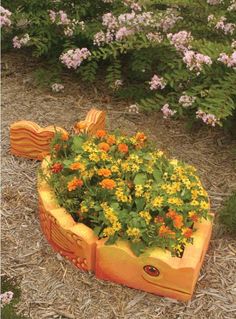 an orange planter filled with yellow flowers on top of dry grass and mulch