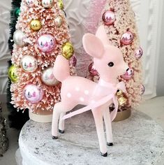 a pink deer figurine sitting on top of a white marble table next to christmas trees