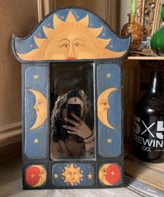 a woman taking a selfie in a mirror with sun and moon painted on it