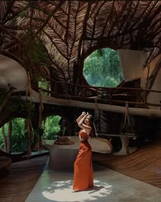 a woman in an orange dress is standing under a straw roof and looking up at the sky