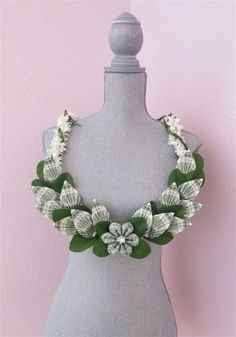 a gray mannequin with white flowers and green leaves on the neck, against a pink wall