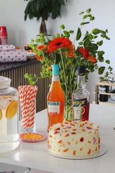 a cake with flowers and drinks sitting on a table next to each other in front of a vase