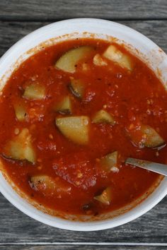 a white bowl filled with vegetable soup on top of a wooden table next to a spoon