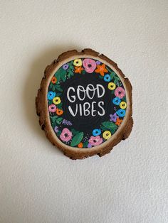 a wooden slice with the words good vibes painted on it, surrounded by flowers