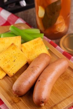 two hot dogs, cheese and celery on a cutting board next to a jar of pickles