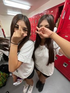 two girls standing in front of lockers making the middle finger sign with their hands