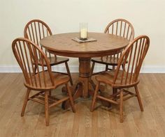 a wooden table with four chairs and a candle on top of it in front of a white wall