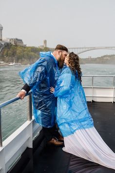 a man and woman in raincoats kissing on a boat deck near the water