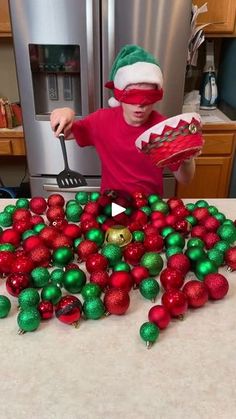 a young boy in a red shirt and green christmas ornaments on a kitchen counter top