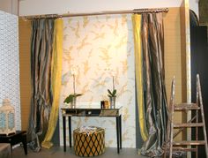 the room is decorated with gold and silver wallpaper, curtains, and a small table