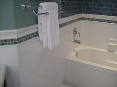 a white bath tub sitting next to a toilet in a bathroom with green tile on the walls