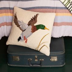 a pillow sitting on top of a piece of luggage next to a bed with a bird embroidered on it