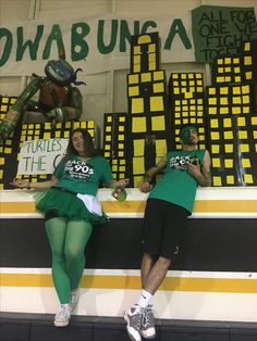 two people dressed up in costumes sitting on a wall with signs reading turtles the turtle